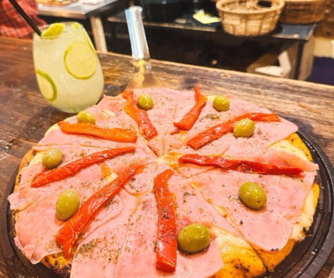 Pizza de jamón y morrón con aceitunas verdes, con una limonada al lado
