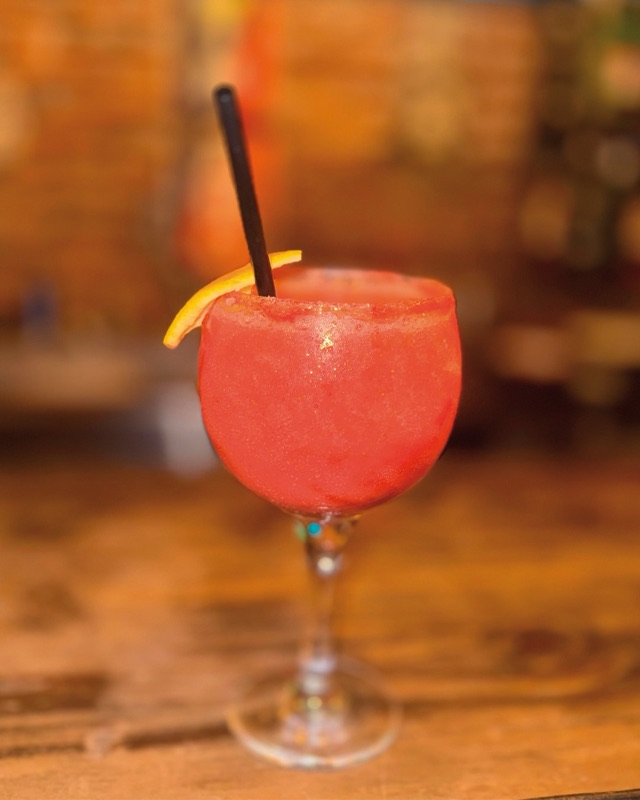 Trago frutal rojo en copa, con una rodaja de naranja